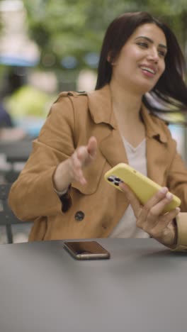 Video-Vertical-De-Una-Pareja-Musulmana-En-Una-Cita-Sentada-En-Una-Mesa-Al-Aire-Libre-En-Una-Calle-De-La-Ciudad-Intercambiando-Números-De-Teléfono